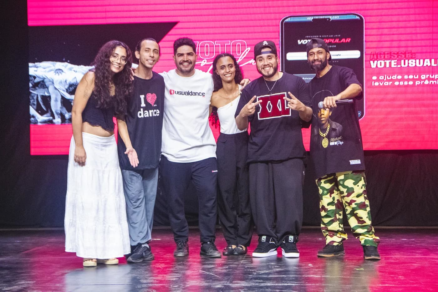 Equipe organizadora da Usualdance Festival 2026 posando no palco ao lado da tela de voto popular